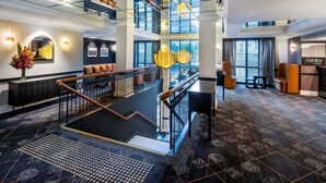 A multi-level hotel lobby with a staircase, seating areas, and large windows. - Mantra on Jolimont Melbourne (East Melbourne)