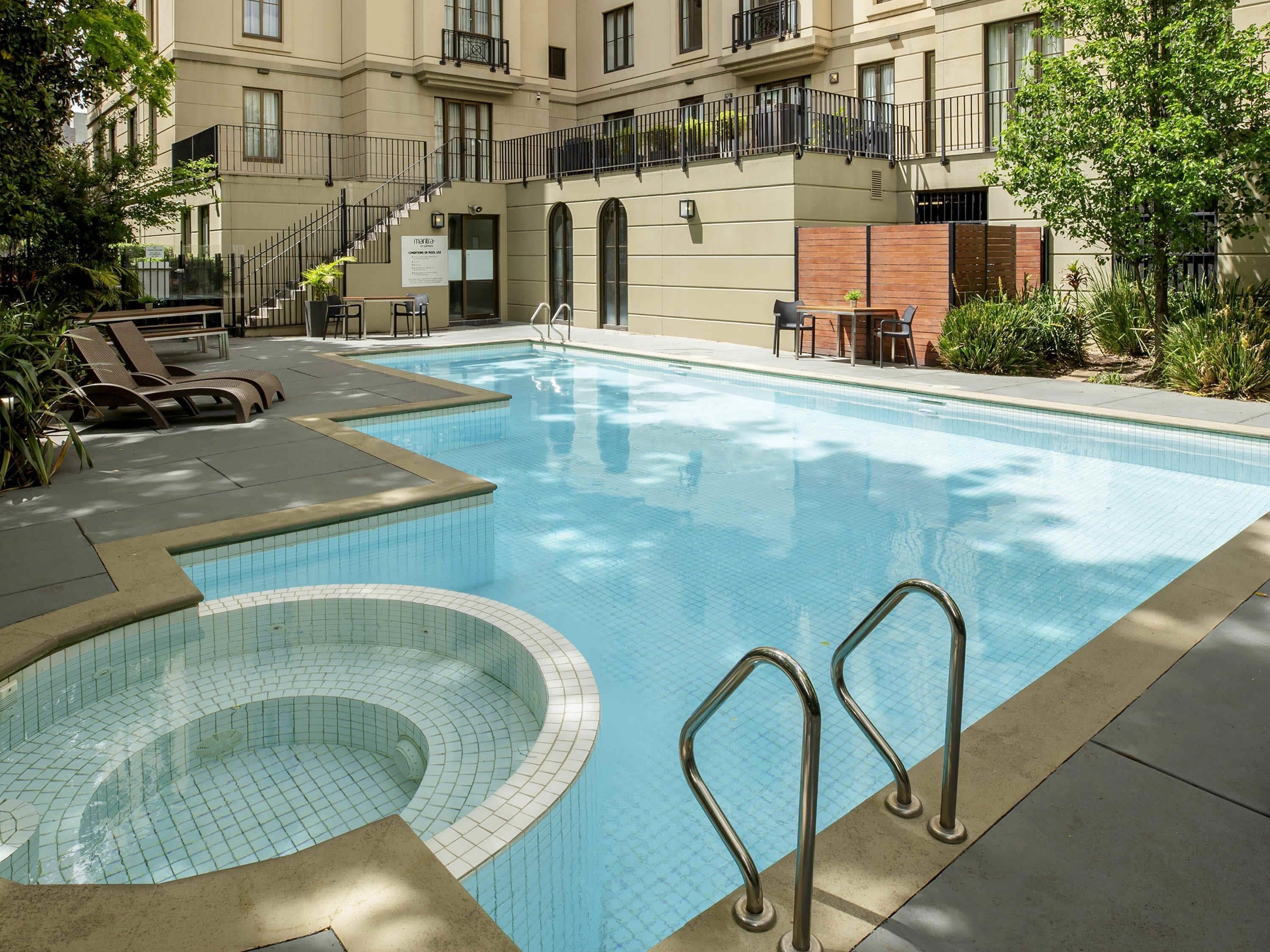 Una piscina con escalones, sillas de descanso y un pequeño jacuzzi.