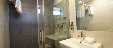 Un baño moderno con ducha de vidrio, lavamanos blanco y un espejo grande.