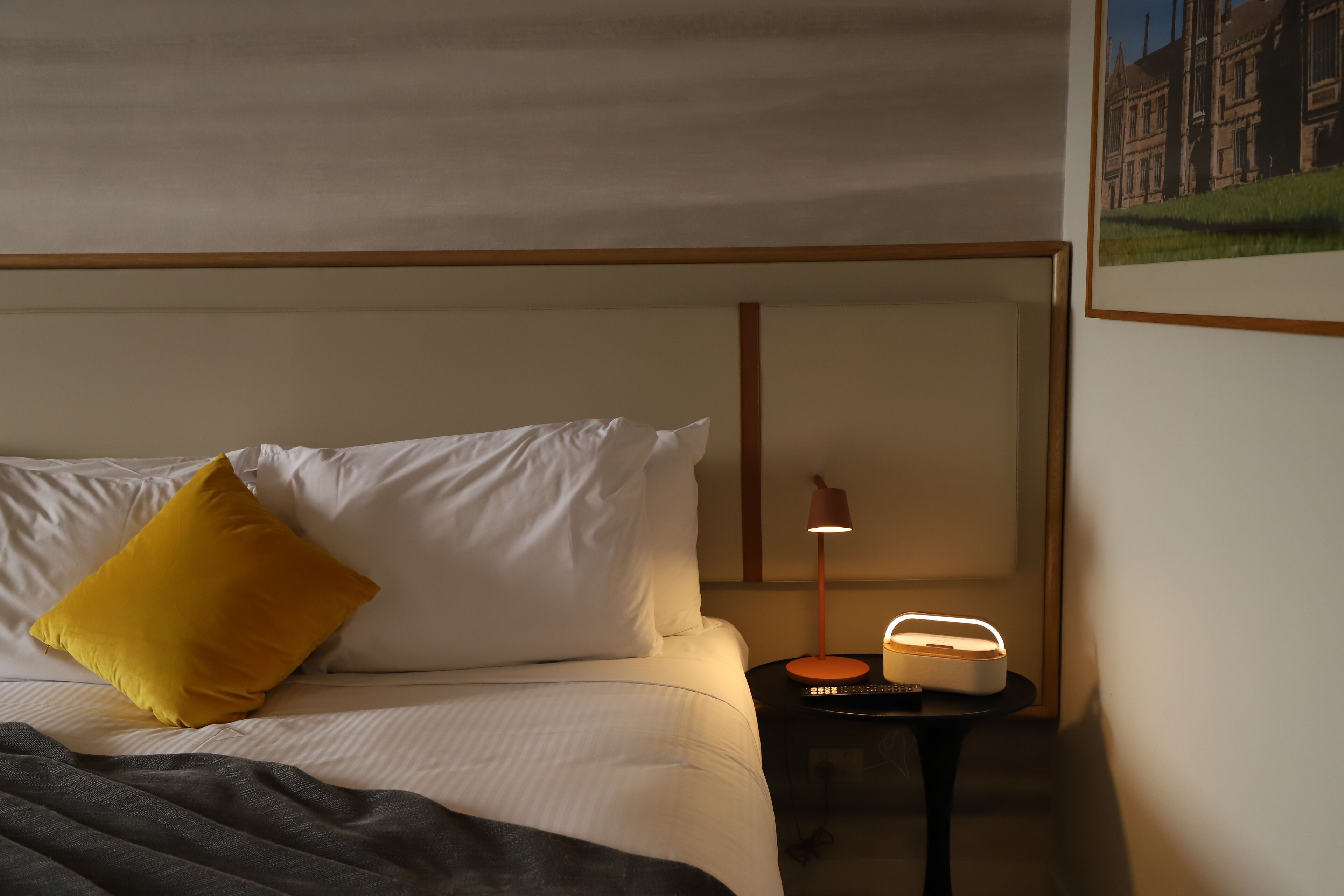 Una habitación de hotel con una cama, una mesita de noche con una lámpara y un cuadro en la pared.
