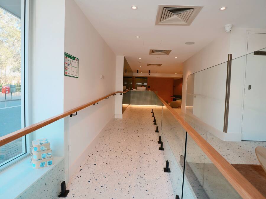 En modern hotellkorridor med ett glasräcke, ett kaklat golv och utsikt över omgivningen.