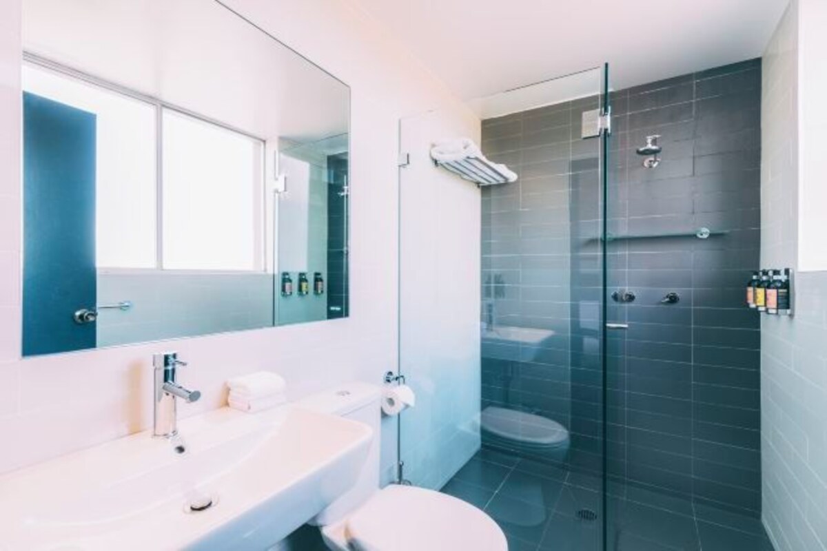 Un baño moderno con ducha vidriada, lavamanos blanco y un espejo grande.