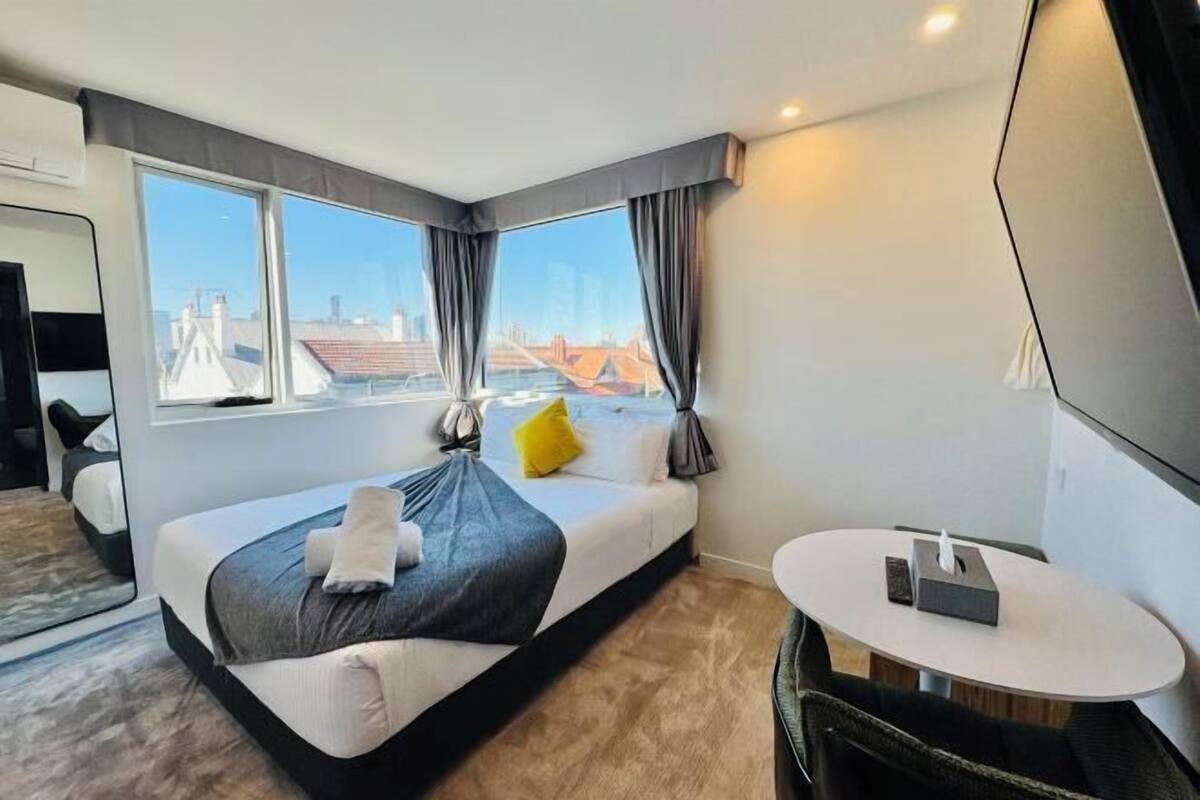 A modern hotel room with a large bed, a small round table, and a view of the cityscape.