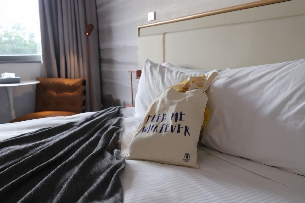 Una habitación de hotel con una cama, un almohadón con texto, una silla y una ventana.
