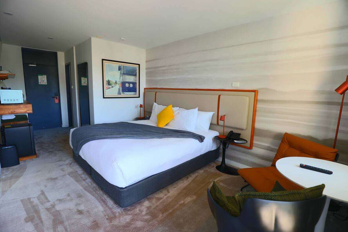 A hotel room with a large bed, a desk with a computer, a chair, and a small table.