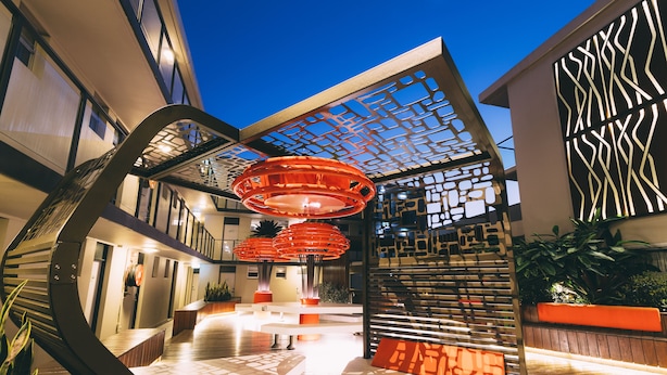 A modern hotel lobby with a geometric ceiling design, a central staircase, and a reception desk. - Haven Glebe (Glebe)
