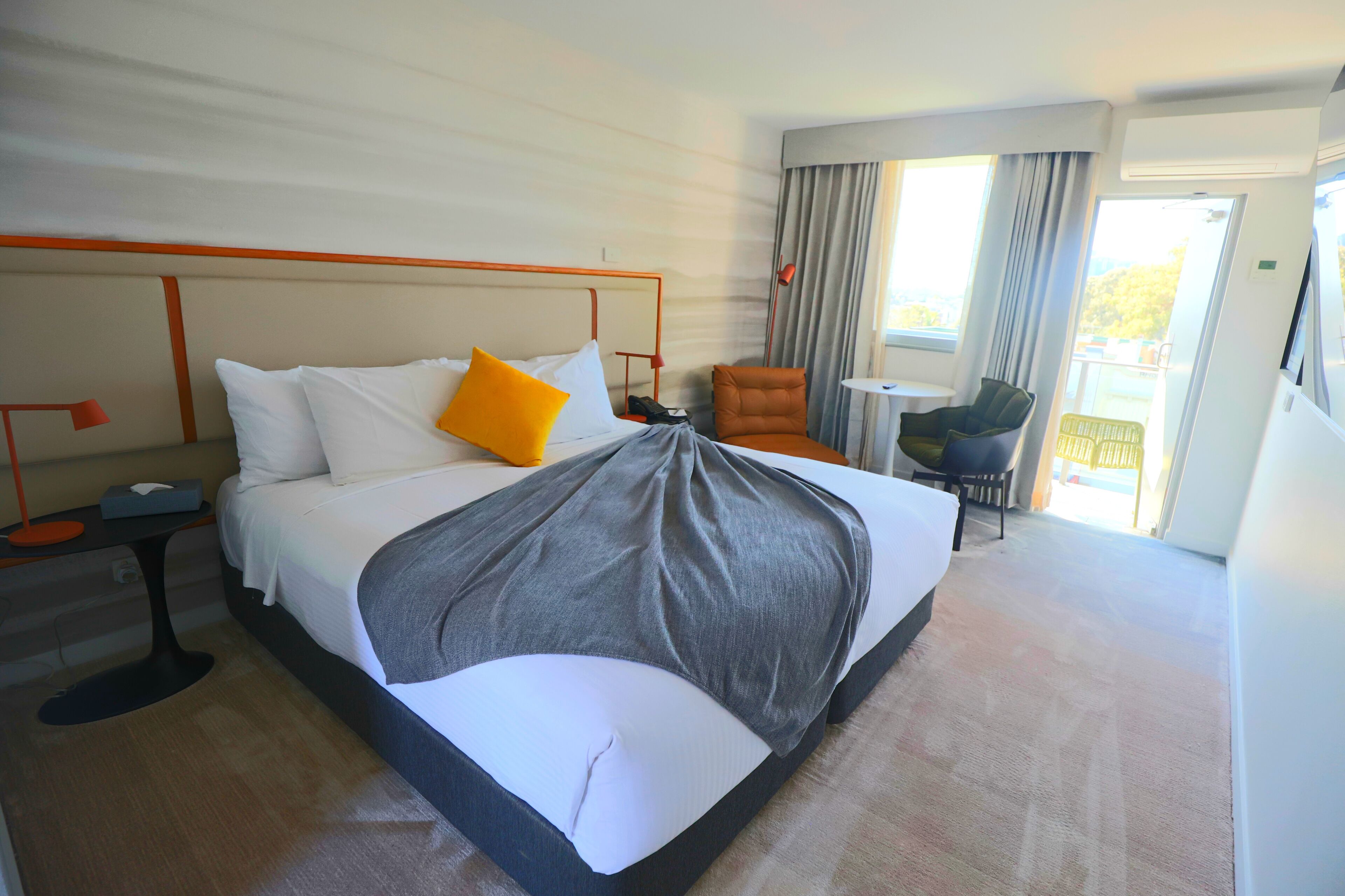Quarto de hotel com uma cama grande, uma cadeira, uma mesa pequena e varanda com vista.