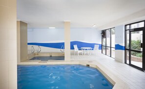 An indoor swimming pool with a view of the outdoors, a seating area with chairs, and a tiled floor. - Breakfree Imperial Surf (Surfers Paradise)