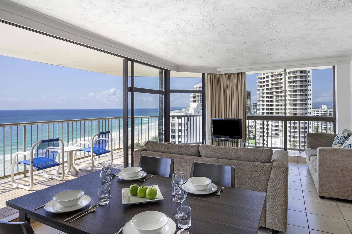 A balcony with a dining table set for two, a sofa, and a TV.