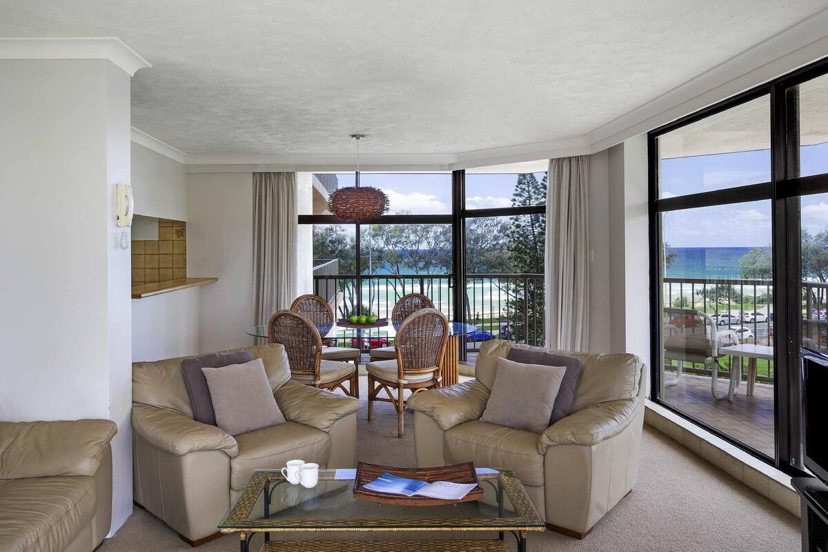A living room with a sofa set, a glass coffee table, and a view of the outdoors.