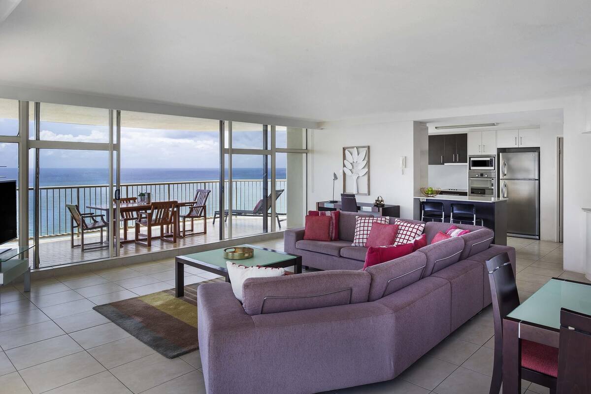 A modern living room with a large sofa, a dining area, and a kitchen.