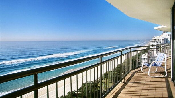 A balcony with a view of the ocean, a white chair, and a building in the background. - Breakfree Imperial Surf (Surfers Paradise)