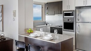 A modern kitchen with a view to the sea, stainless appliances, and a dining area with chairs and a table. - Breakfree Imperial Surf (Surfers Paradise)