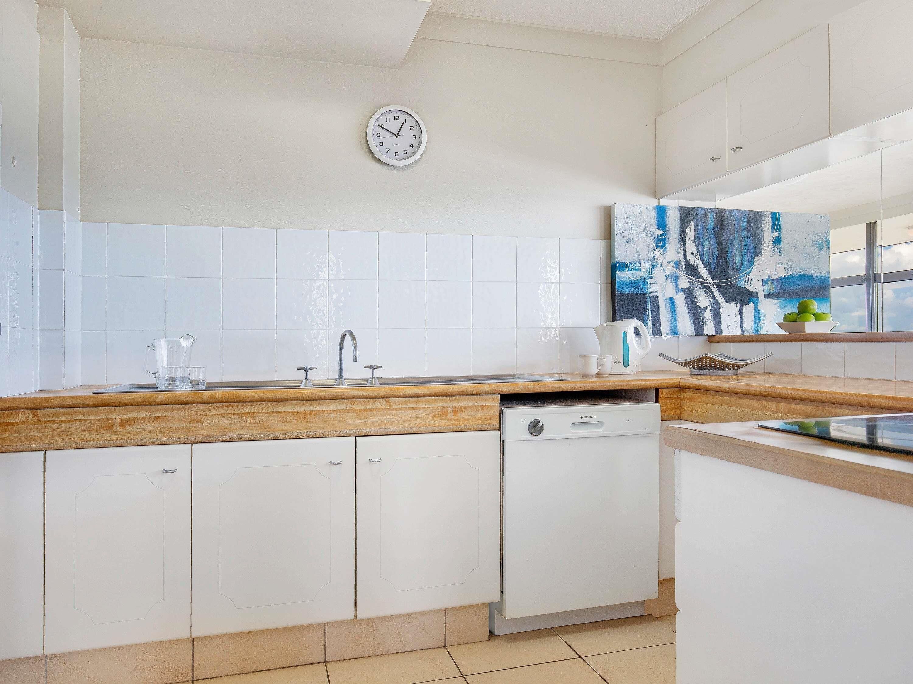A modern kitchen with white cabinetry, a wooden countertop, a dishwasher, and a clock on the wall.