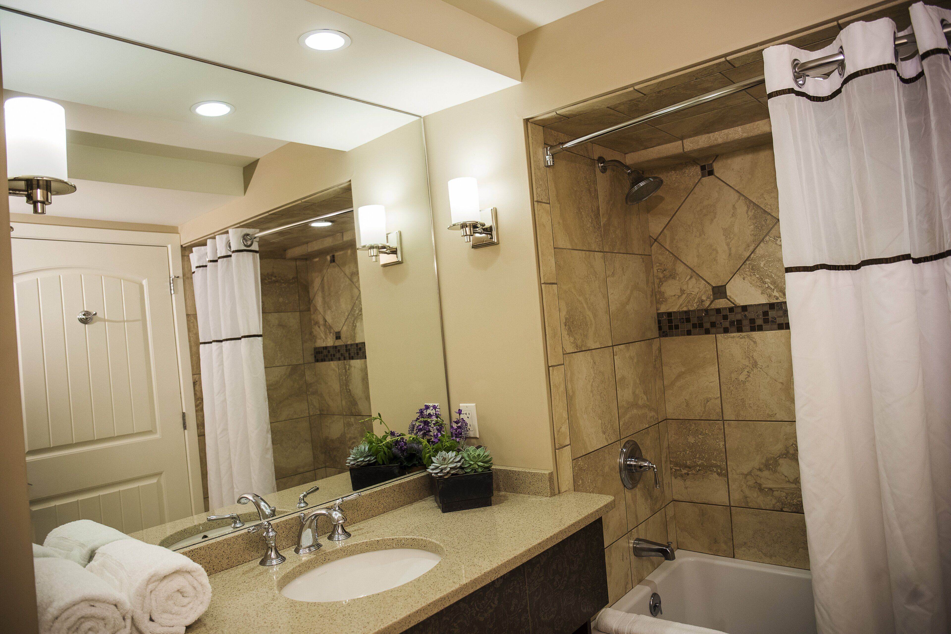 A modern bathroom with a sink, mirror, shower, and towel rack.