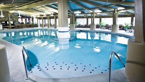 An indoor swimming pool with a blue tiled floor, surrounded by lounge chairs and tables, under a blue-tiled roof. - Lake Lawn Resort (Delavan)