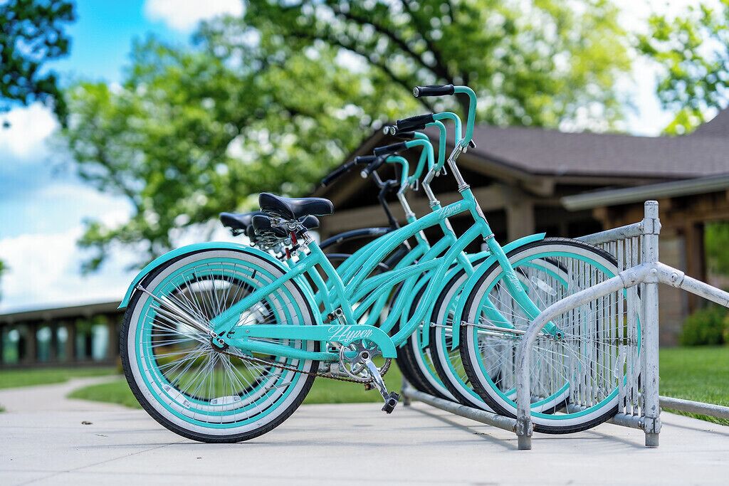 Una bicicleta turquesa con asiento y manillar negros, sujeta a un portaequipajes metálico al aire libre.
