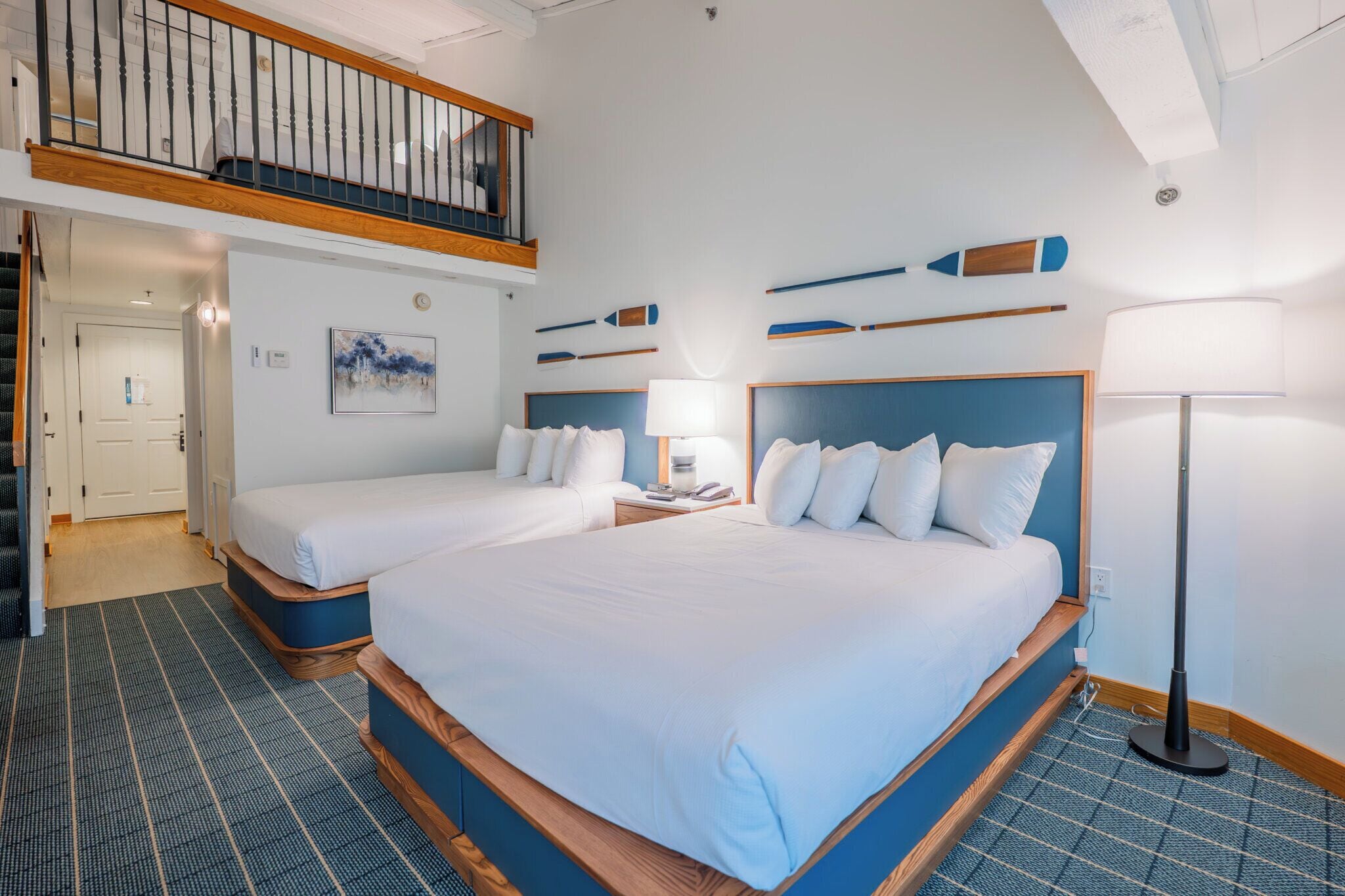 A hotel room with two beds, a balcony, a painting, and a lamp.