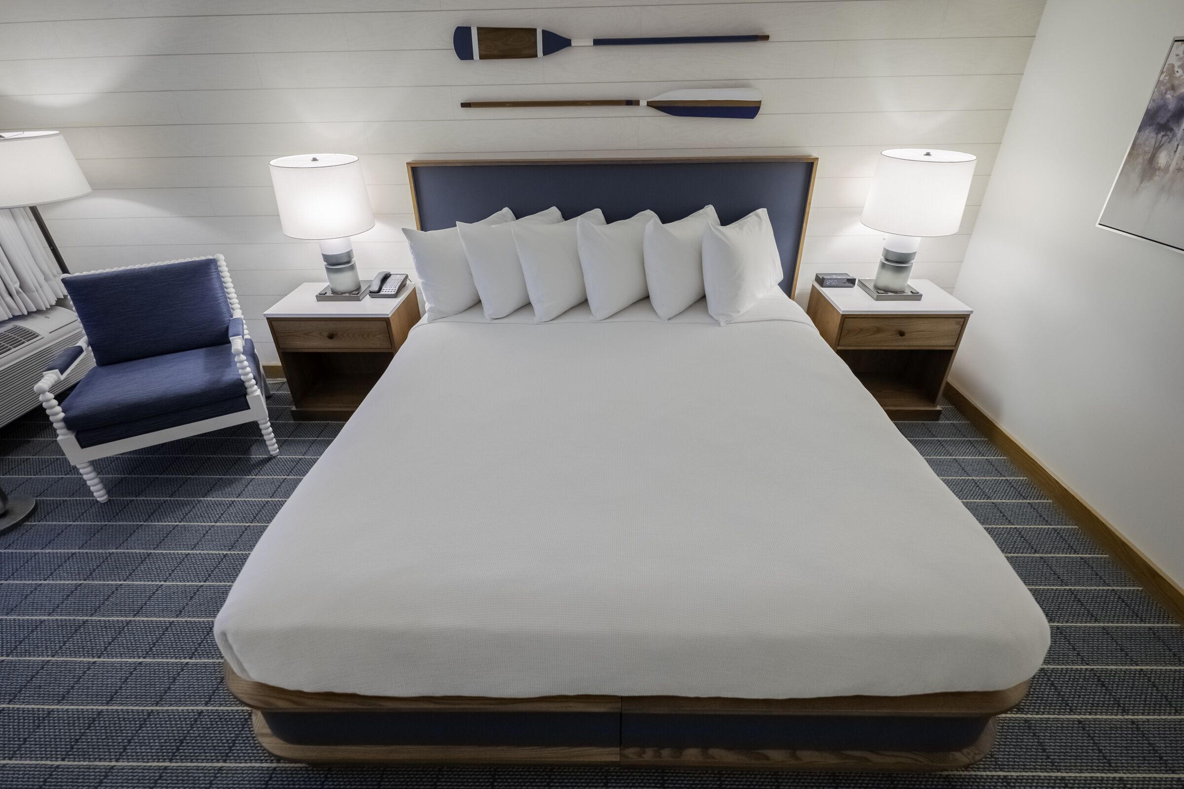 A hotel room with a large bed, two bedside tables, a chair, and a headboard with decorative elements.