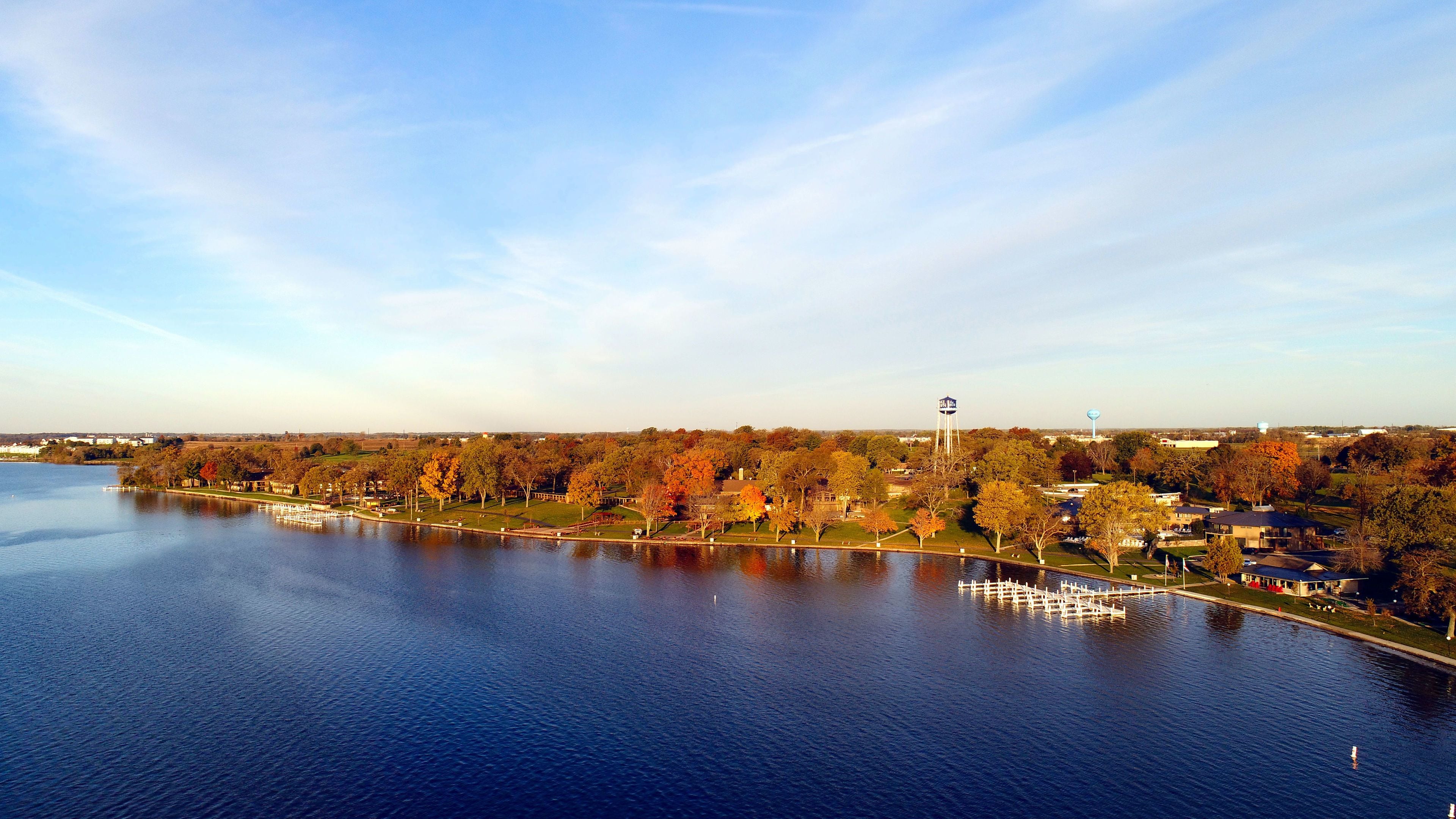 Blick auf einen See mit einem Park, einem Wasserturm und einem Gebäude in der Ferne.