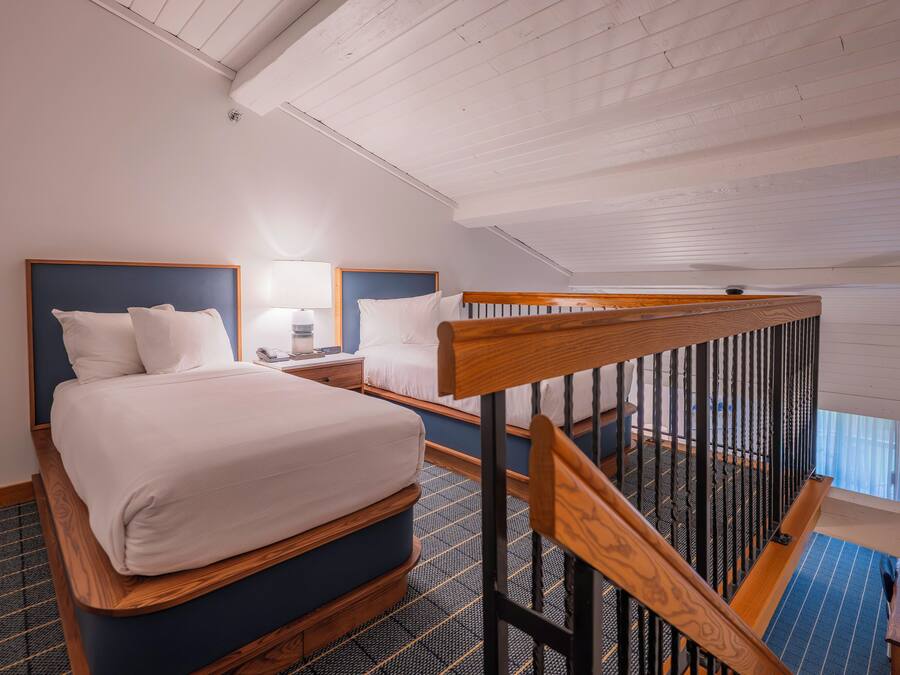 Habitación de hotel con cama, mesita de noche, lámpara y vista al exterior.