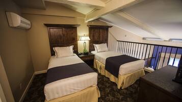 A hotel room with two beds, a desk, a lamp, and a staircase.