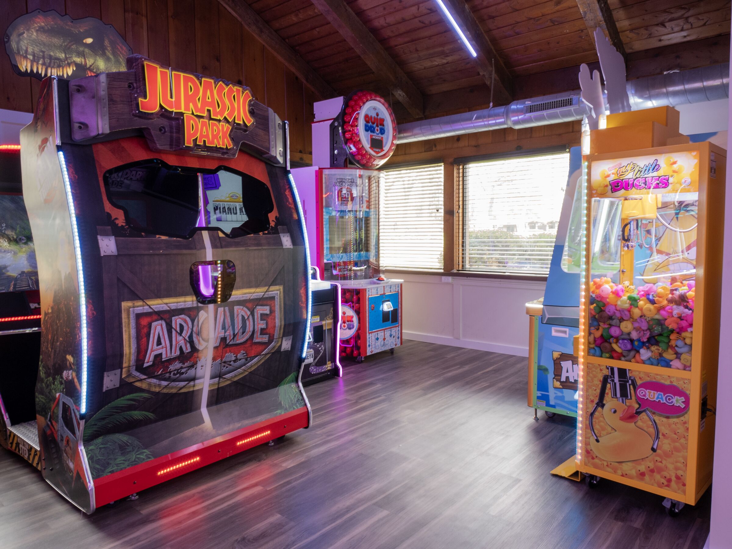 A room with arcade games, including a 'Jurassic Park' game, a 'Quiz Dozer' game, and a 'Duck Quack' game.