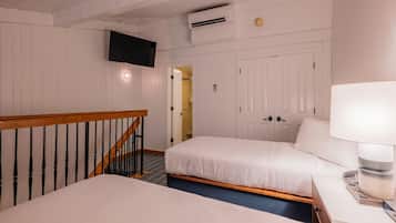 Een hotelkamer met twee bedden, een aan de muur bevestigde televisie, een airconditioning en een trap naar een andere kamer.