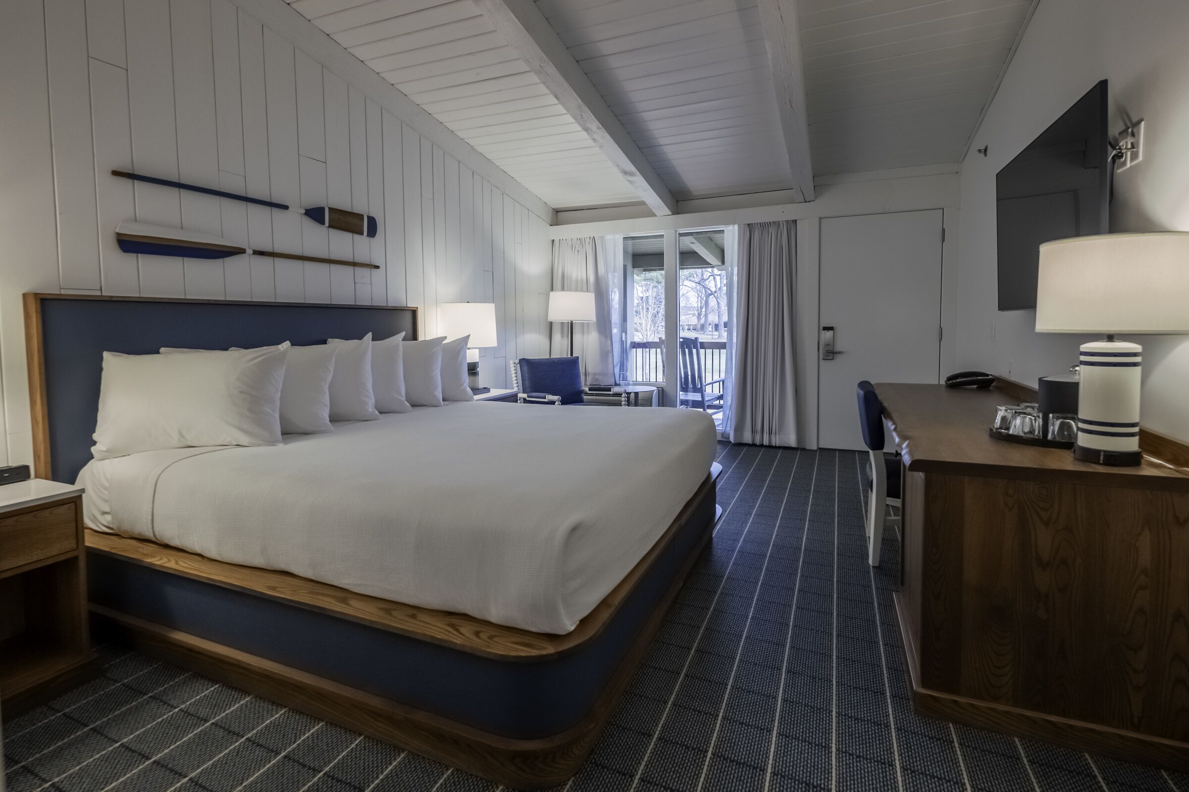 A hotel room with a large bed, a desk, a chair, and a view of the outdoors.