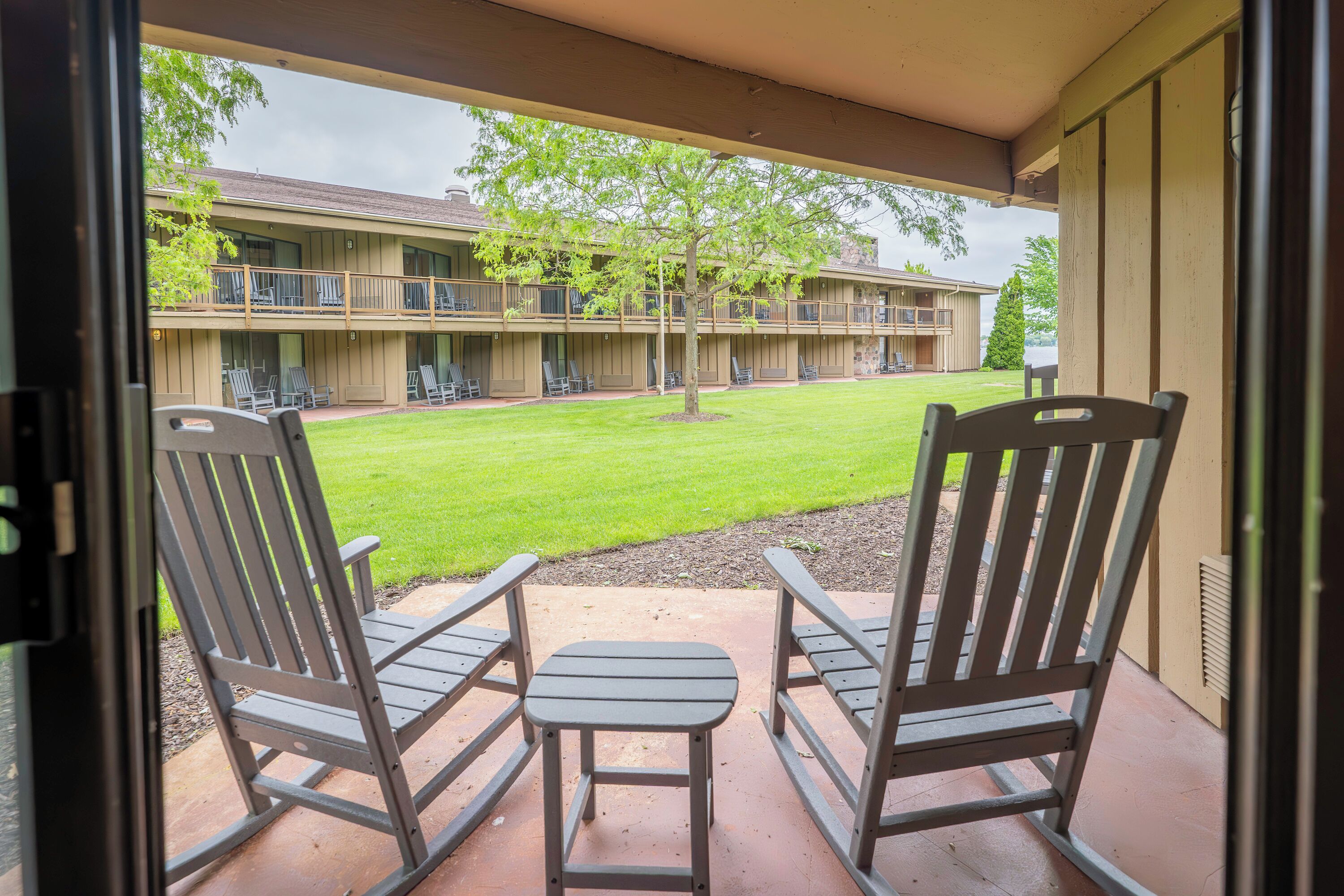 A patio with two rocking chairs and a small table, overlooking a building with multiple balconies and a lawn.