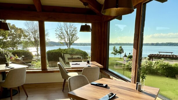 A dining area with a wooden table and chairs, large windows offering a view of a lake and greenery. - Lake Lawn Resort (Delavan)