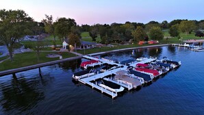 A marina with boats docked, a grassy area with a building, and trees in the background. - Lake Lawn Resort (Delavan)