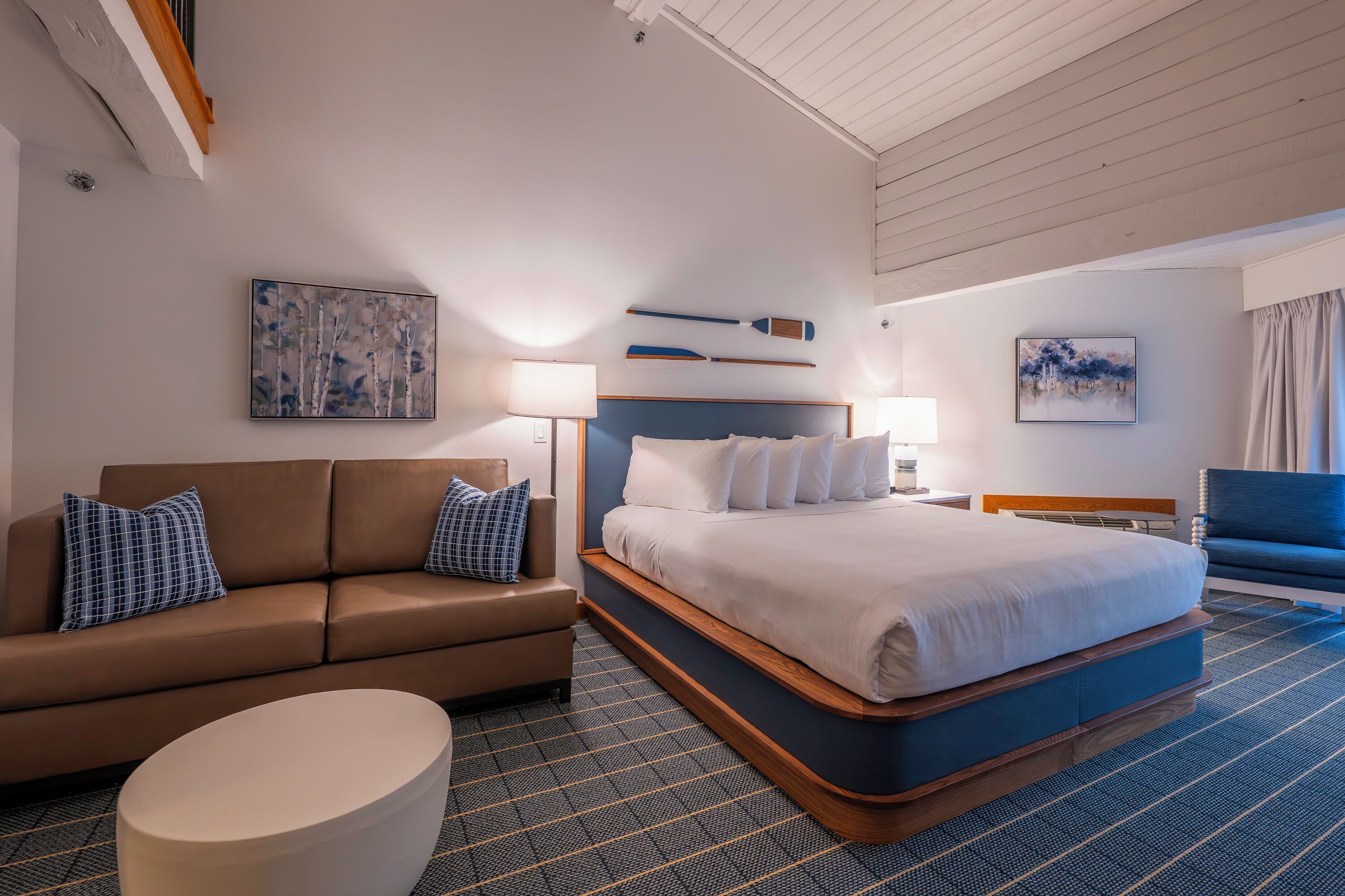 A modern hotel room with a large bed, a sofa, and a small round table.