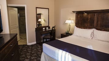 Ein Hotelzimmer mit Bett, Schreibtisch, Stuhl, Kommode, Spiegel und Nachttisch mit Lampe.
