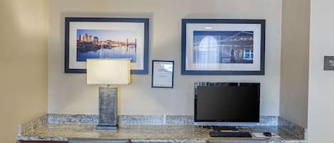 A hotel reception desk with framed cityscape pictures, a desk lamp, a flat-screen TV, and a computer.
