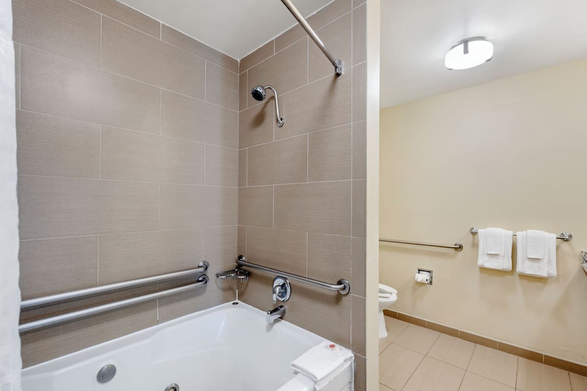 A modern bathroom with a bathtub, shower, and handrails.