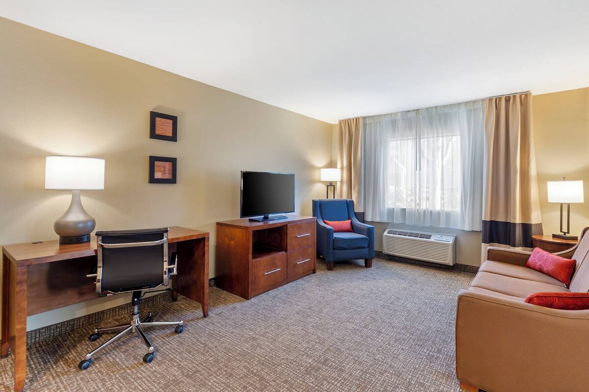 A hotel room with a desk, chair, television, and a sofa.