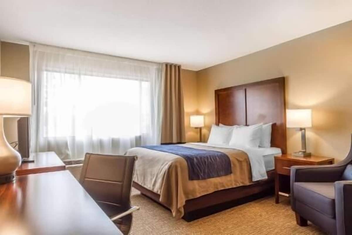 A hotel room with a bed, two bedside tables, a desk, a chair, and a window with curtains.