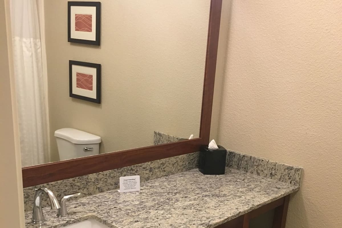 A bathroom with a granite countertop sink, a mirror, a toilet, and a towel rack.