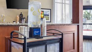 Uma área de recepção de hotel com um dispensador de bebidas de serviço próprio, uma TV de tela plana e uma grande janela com vista para o exterior.