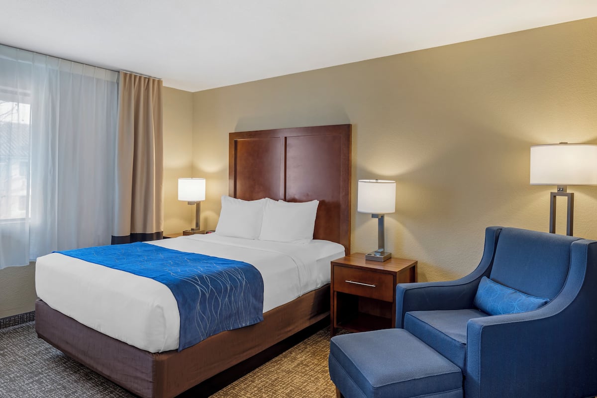 A hotel room with a large bed, two bedside tables with lamps, a chair, and a window with curtains.