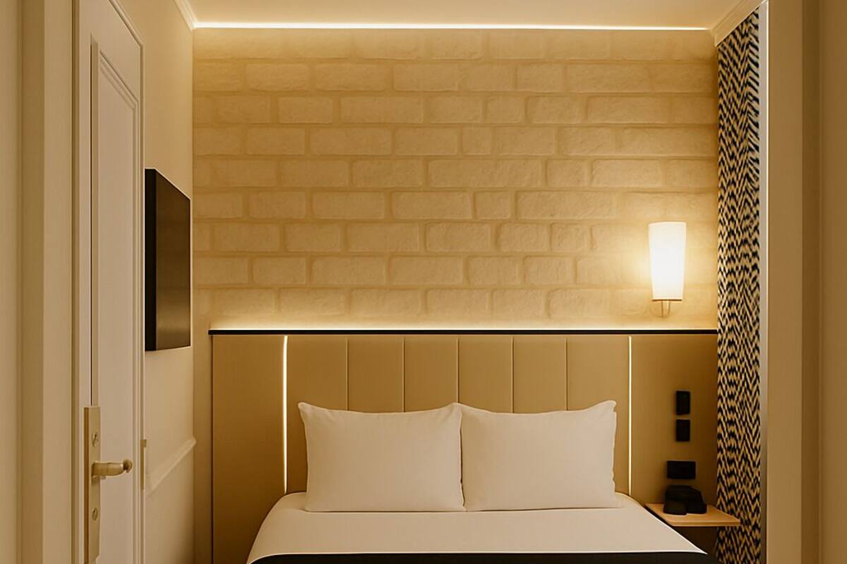 A hotel room with a large bed, a brick-patterned wall, a flat-screen TV, and a nightstand with a lamp.
