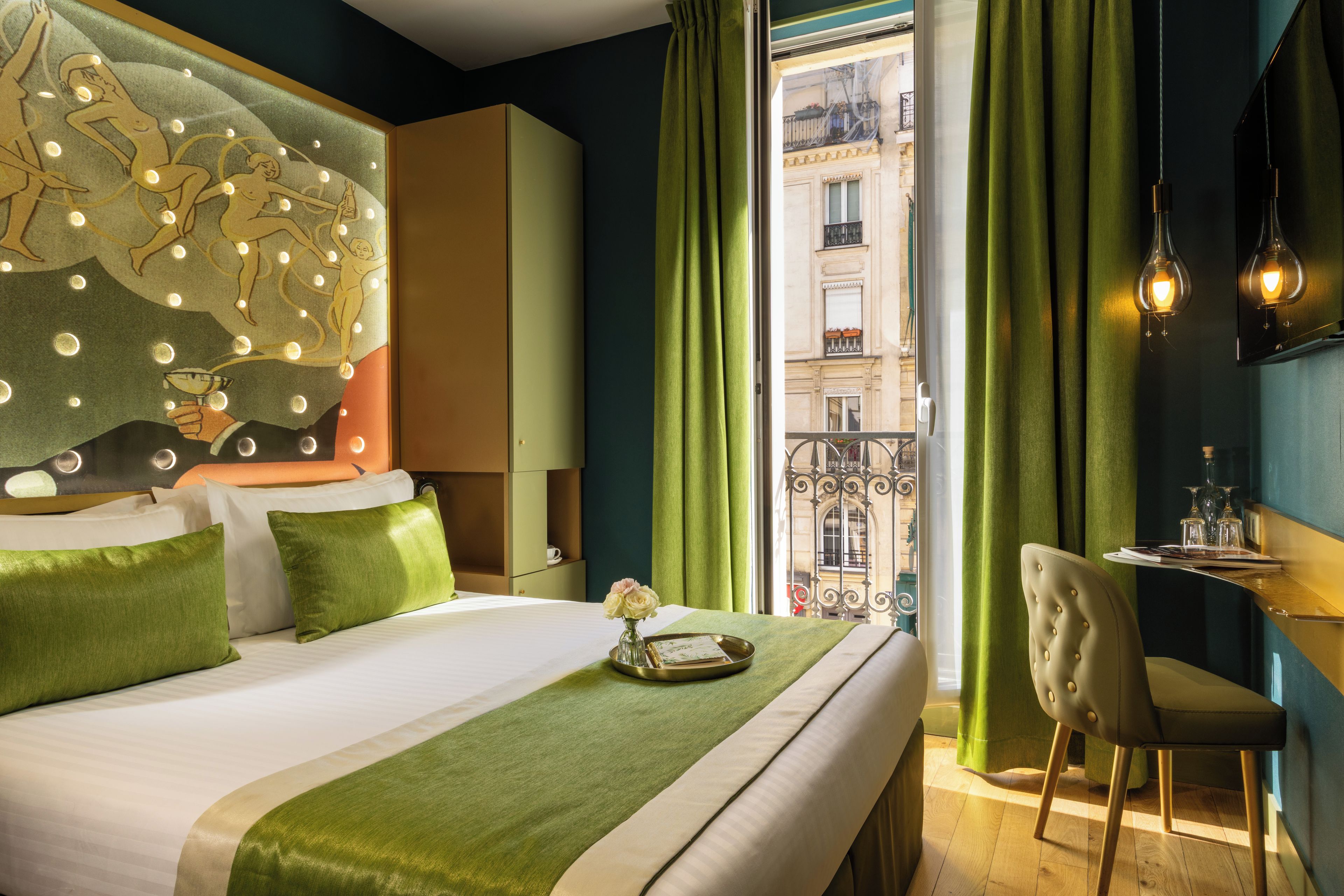 Une chambre d’hôtel avec un lit, une chaise, une table avec des verres et une vue sur un immeuble par la fenêtre.