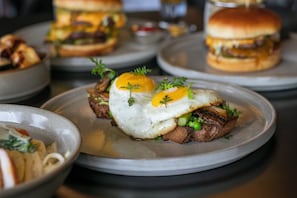 A plate with a sandwich topped with a fried egg, greens, and mushrooms.