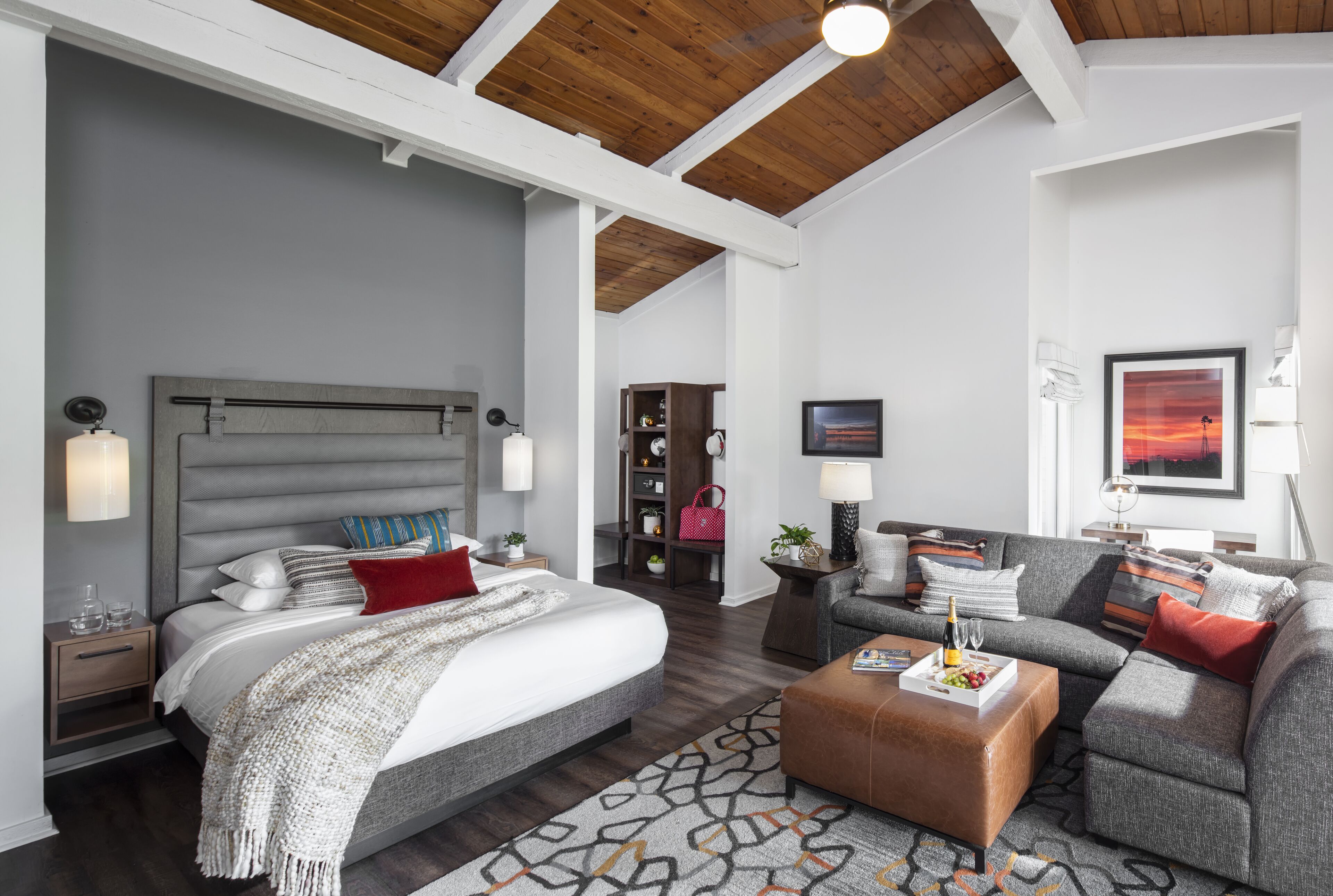 A modern bedroom with a large bed, a sofa, and a coffee table. There is a wooden ceiling and a painting on the wall.