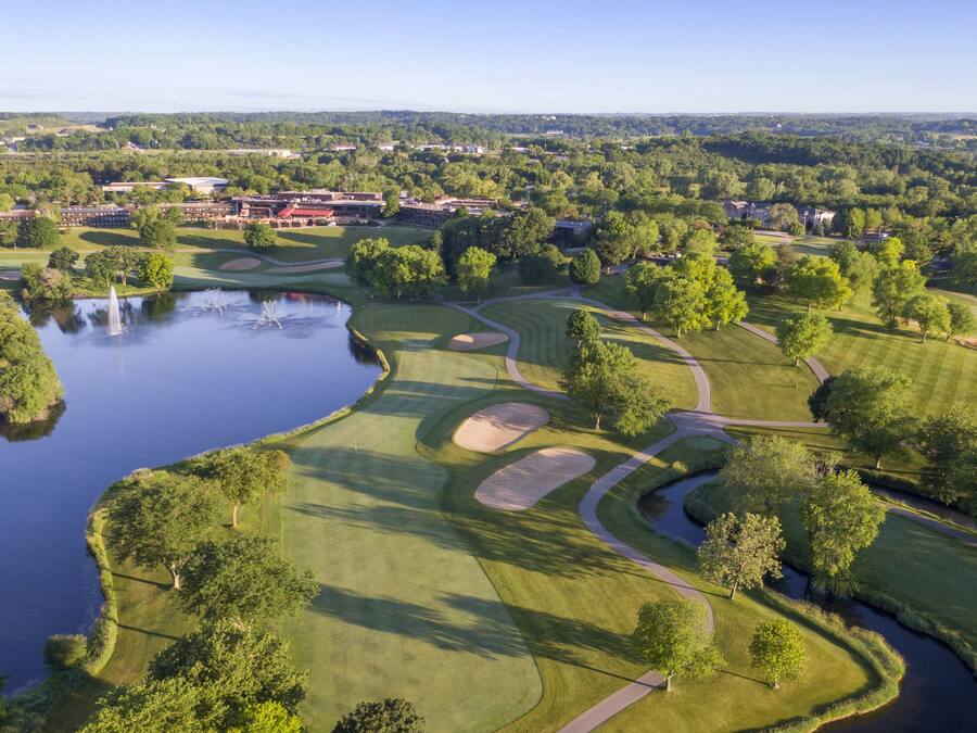 A golf course with a pond, trees, and a distant town.