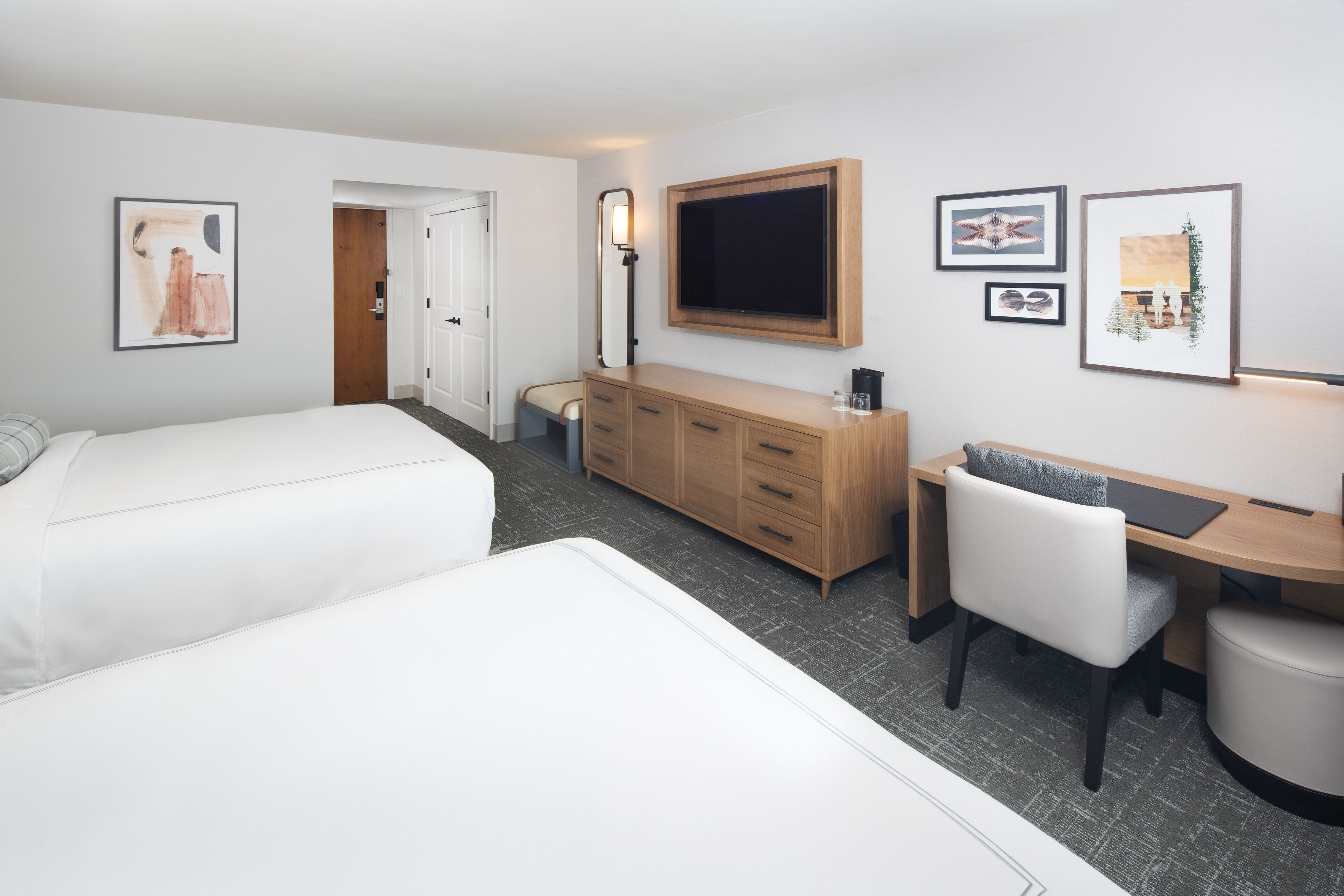 A hotel room with two beds, a desk, a chair, a dresser, and a flat-screen TV.