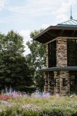 A stone tower with a green roof, surrounded by a garden with various flowers and trees.
