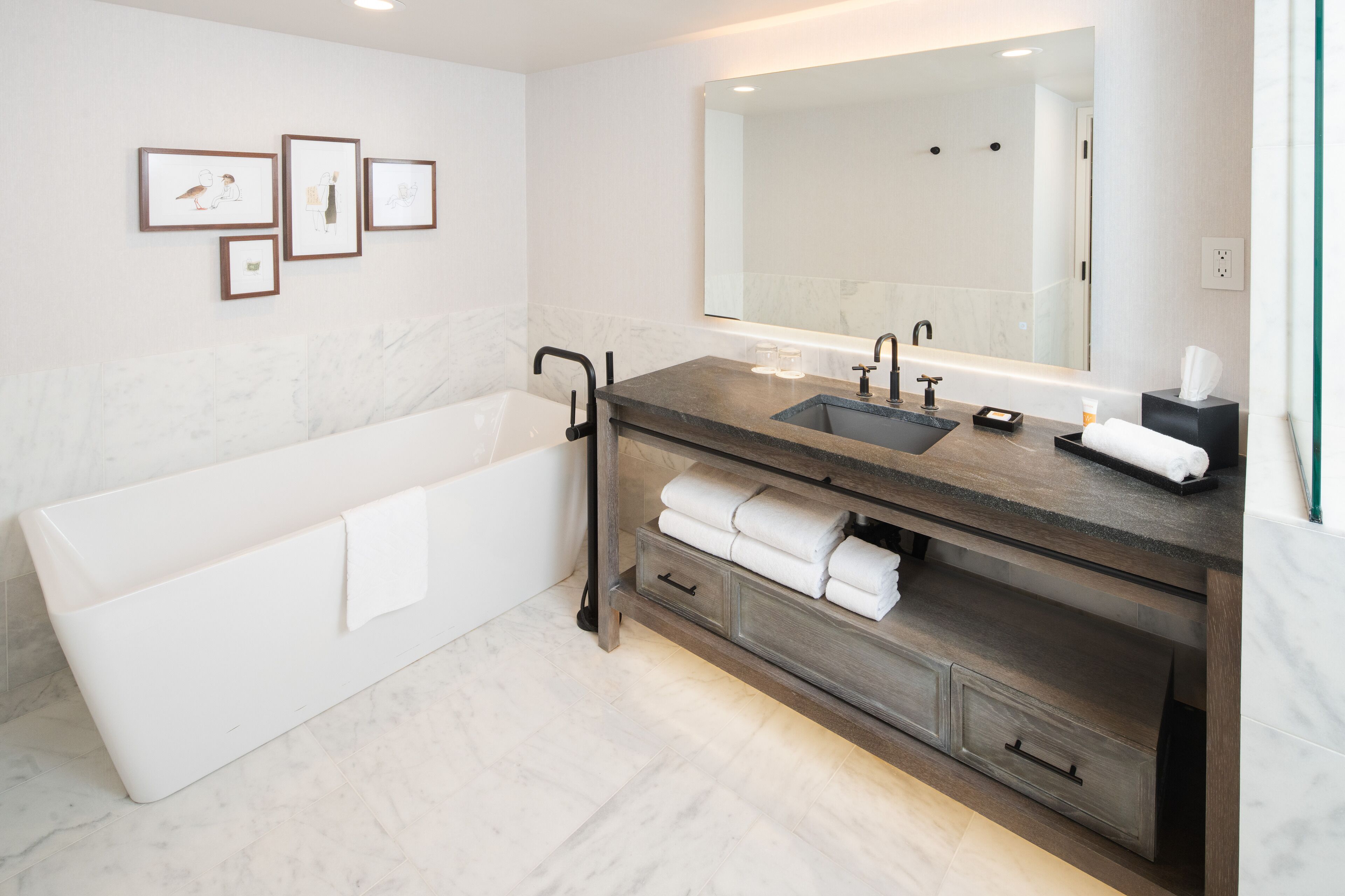 A modern bathroom with a bathtub, a large mirror, and a vanity with a sink and towel storage.