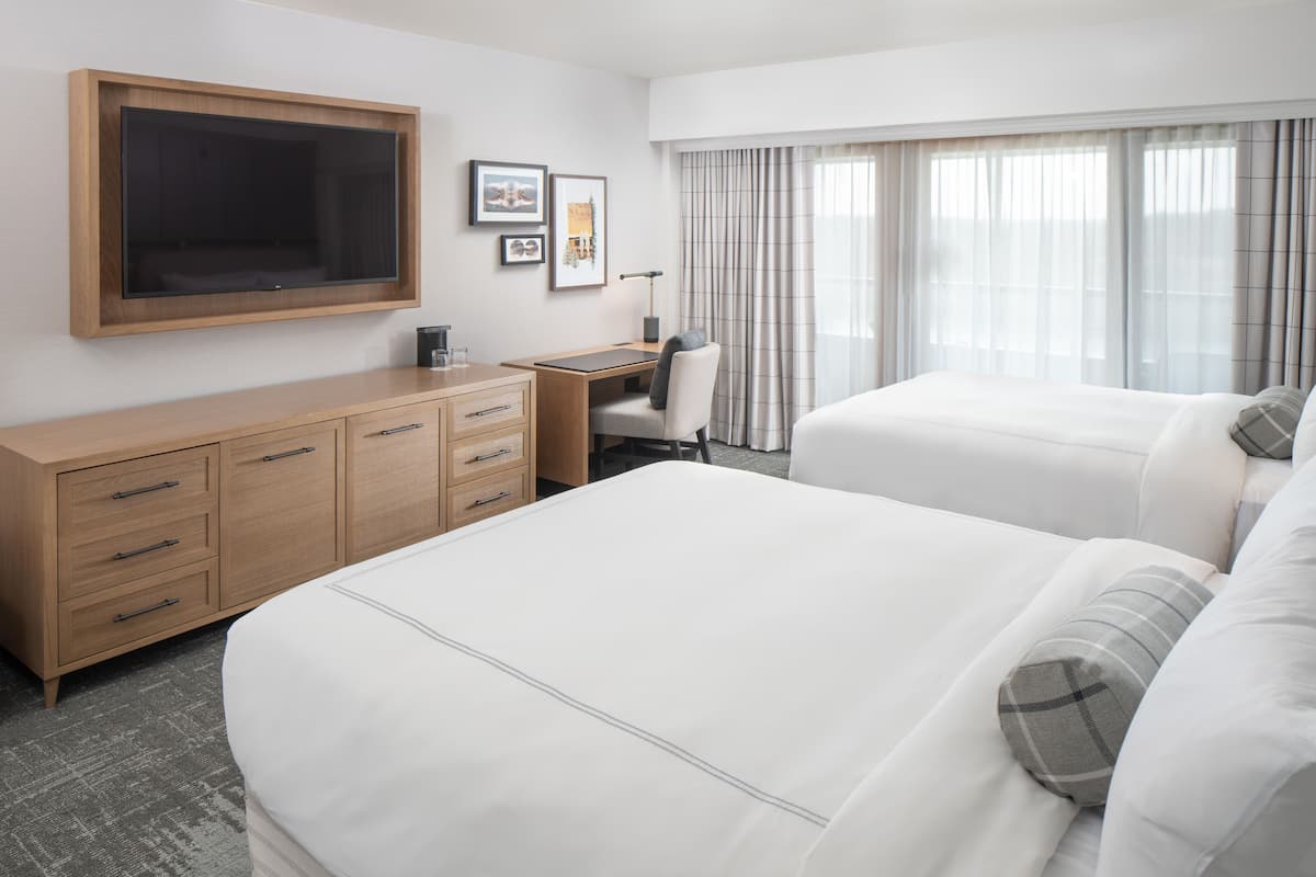 A hotel room with a large bed, a desk, a chair, a TV, and a wardrobe.
